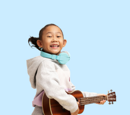 Child playing a ukulele while wearing headphones at The Music Scientist music class